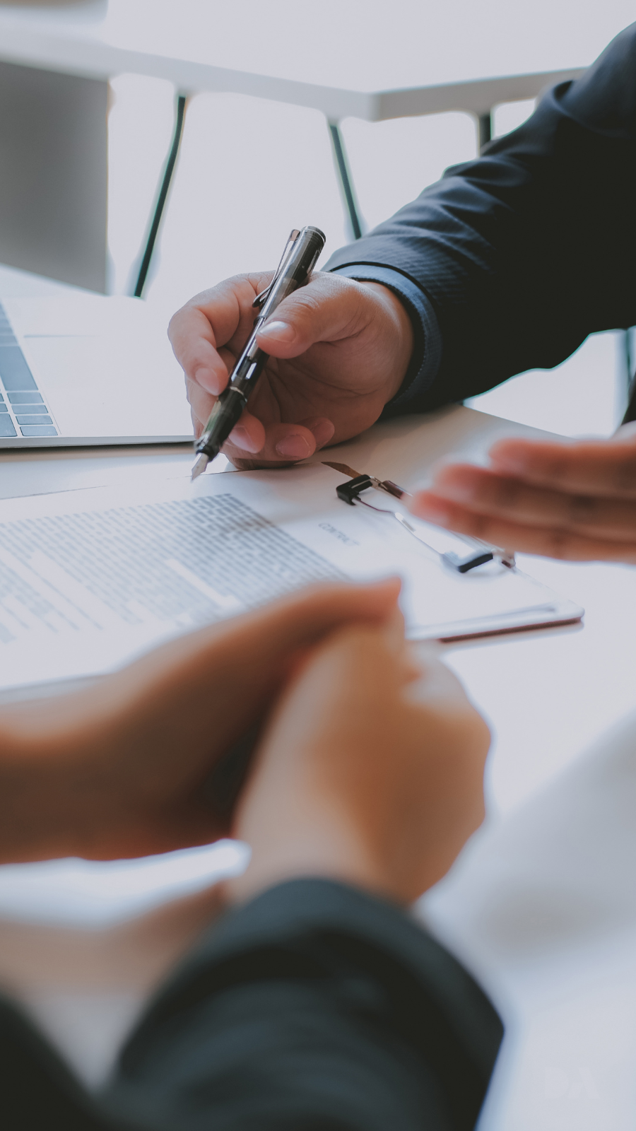 Mortgage broker with contract and laptop on desk as two people discuss the agreement
